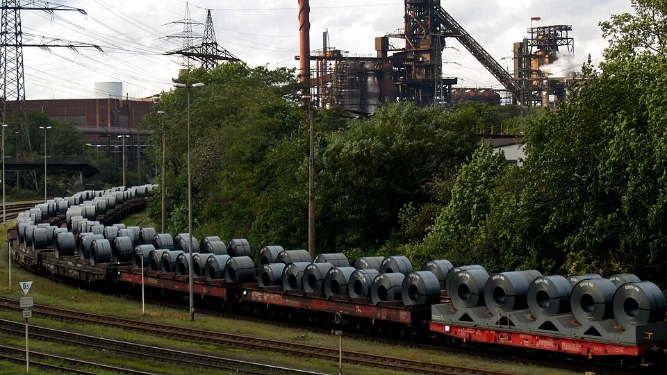 Steel coils loaded on rail wagons with a steel mill in the background